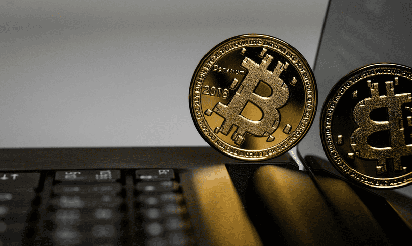 عملة بيتكوين (Bitcoin) بلون ذهبي تستند إلى شاشة حاسب محمول