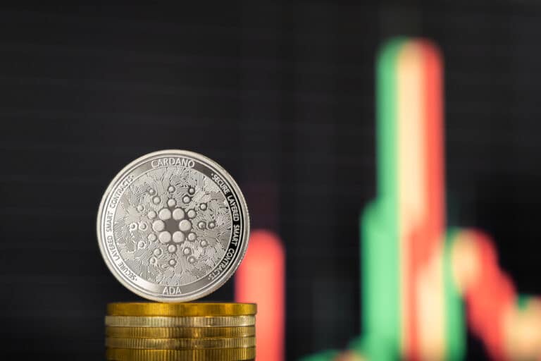 عملة كاردانو (Cardano) معدنية خلفها شاشة يظهر عليها مخطط بياني