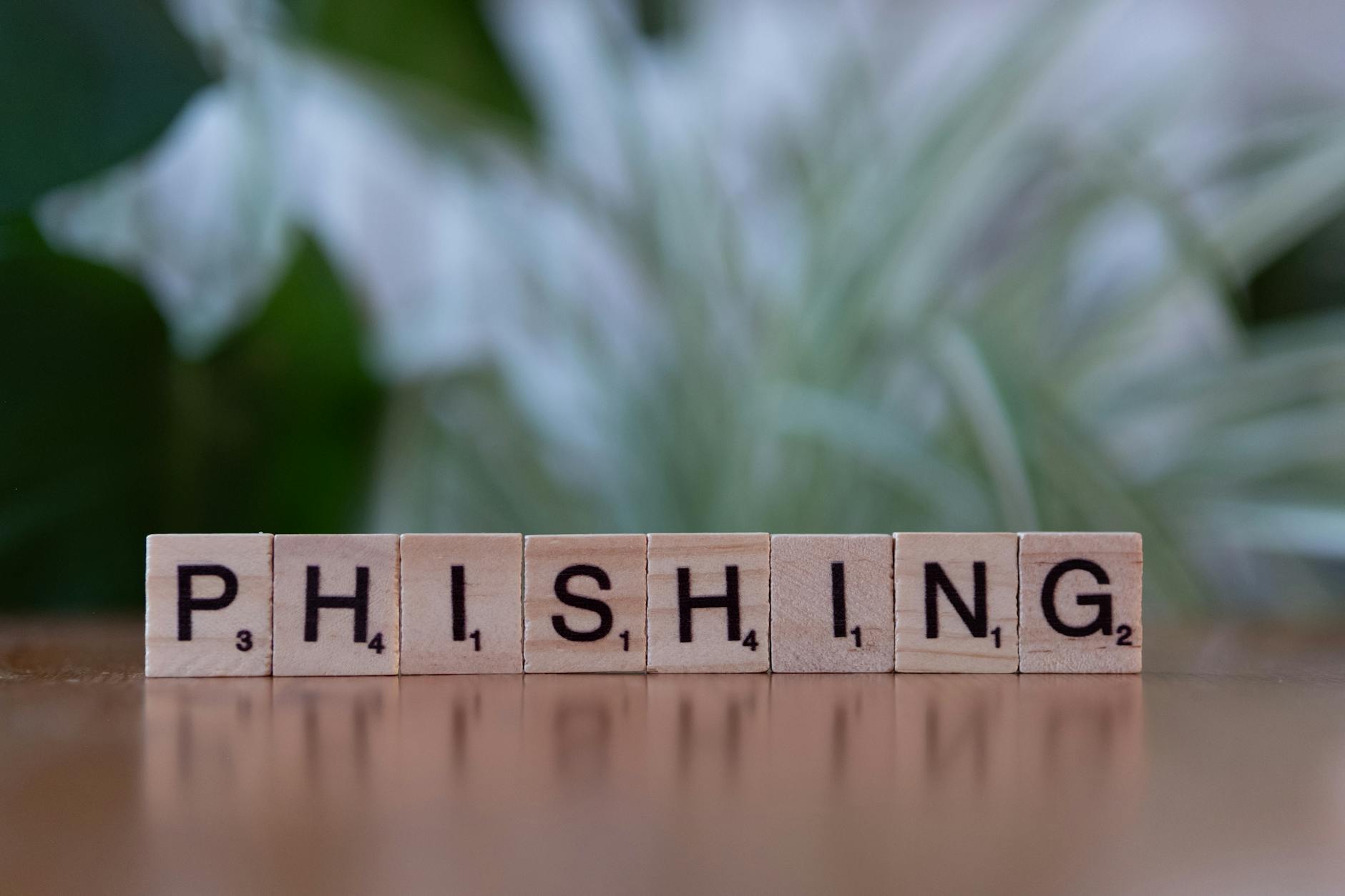 Scrabble tiles spelling 'PHISHING' on a wooden table with a blurred background.