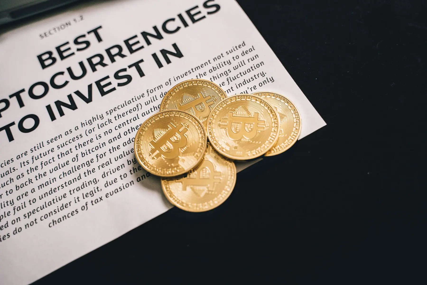 Physical gold-colored Bitcoin coins resting on a printed document titled 'Best Cryptocurrencies to Invest In'