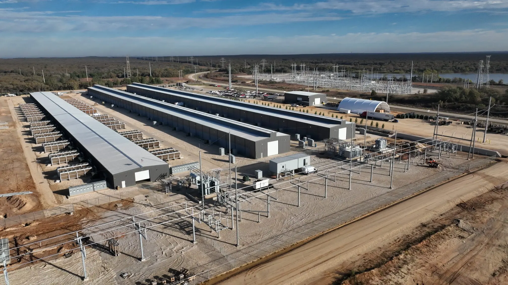 Aerial view of a large industrial bitcoin mining facility with multiple long warehouses and electrical substations