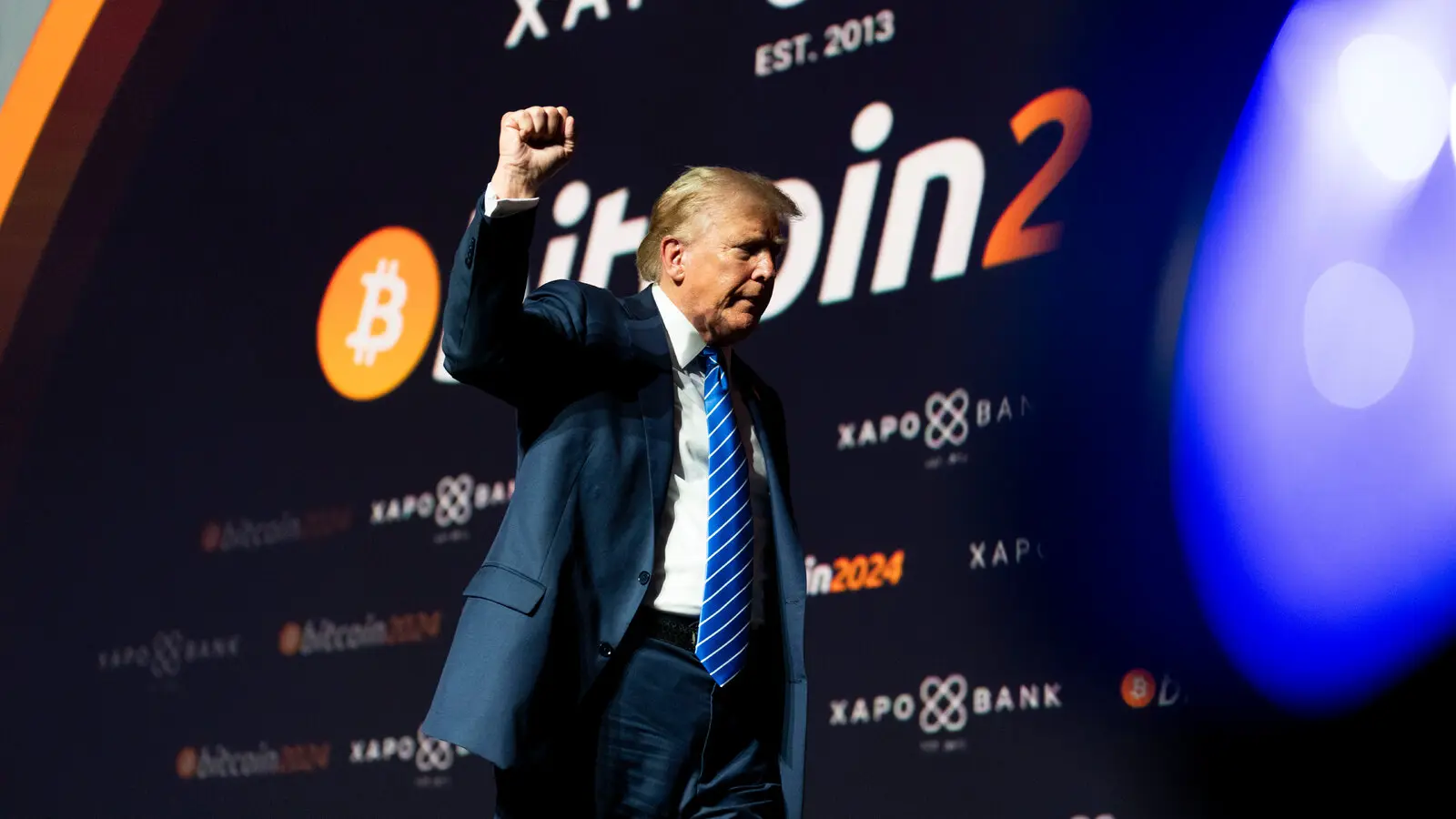 Donald Trump speaking at a podium with a large Bitcoin 2024 backdrop and Bitcoin logo