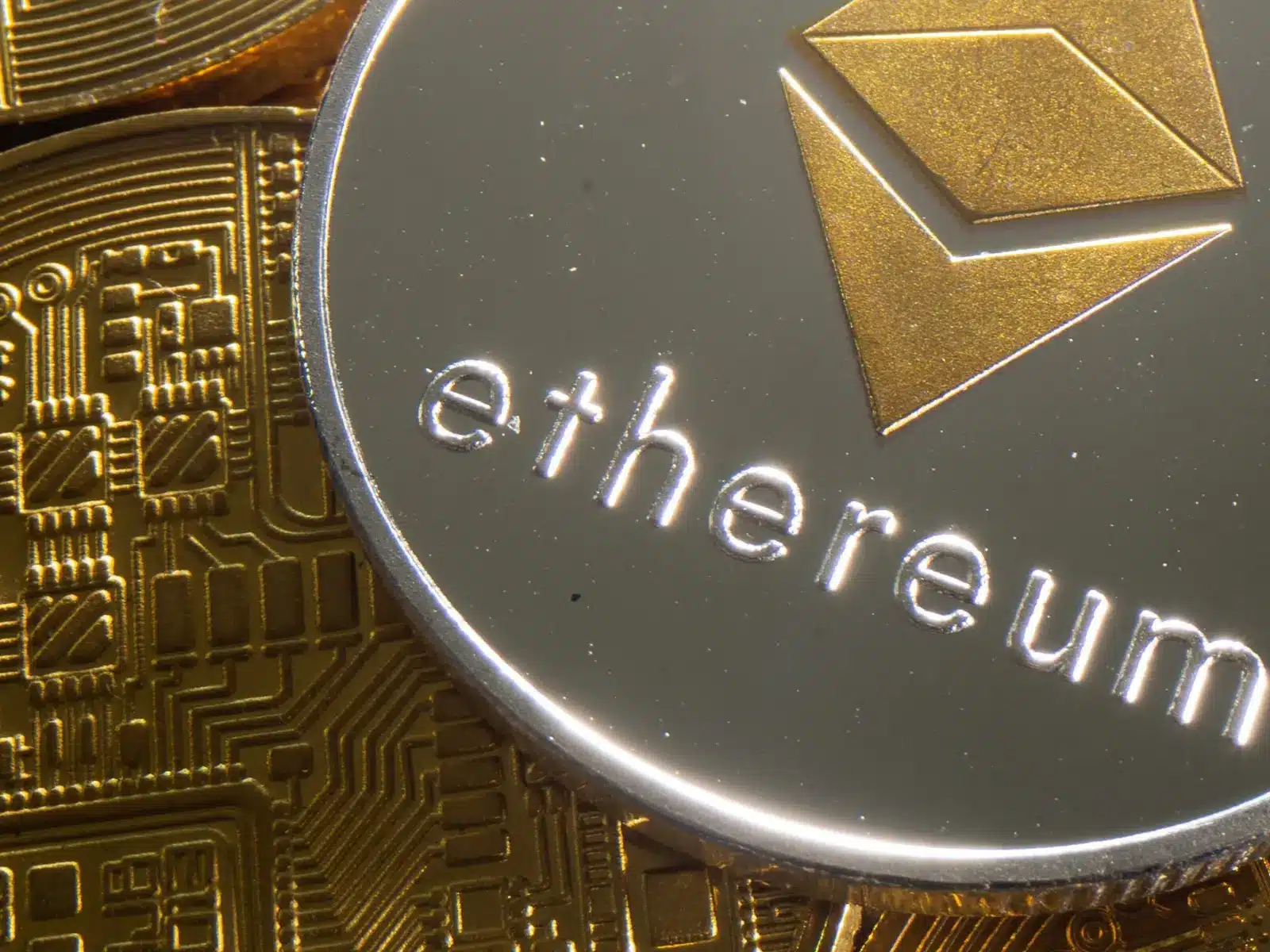 Close-up of a silver Ethereum token with the logo and name on top of gold circuit-patterned coins