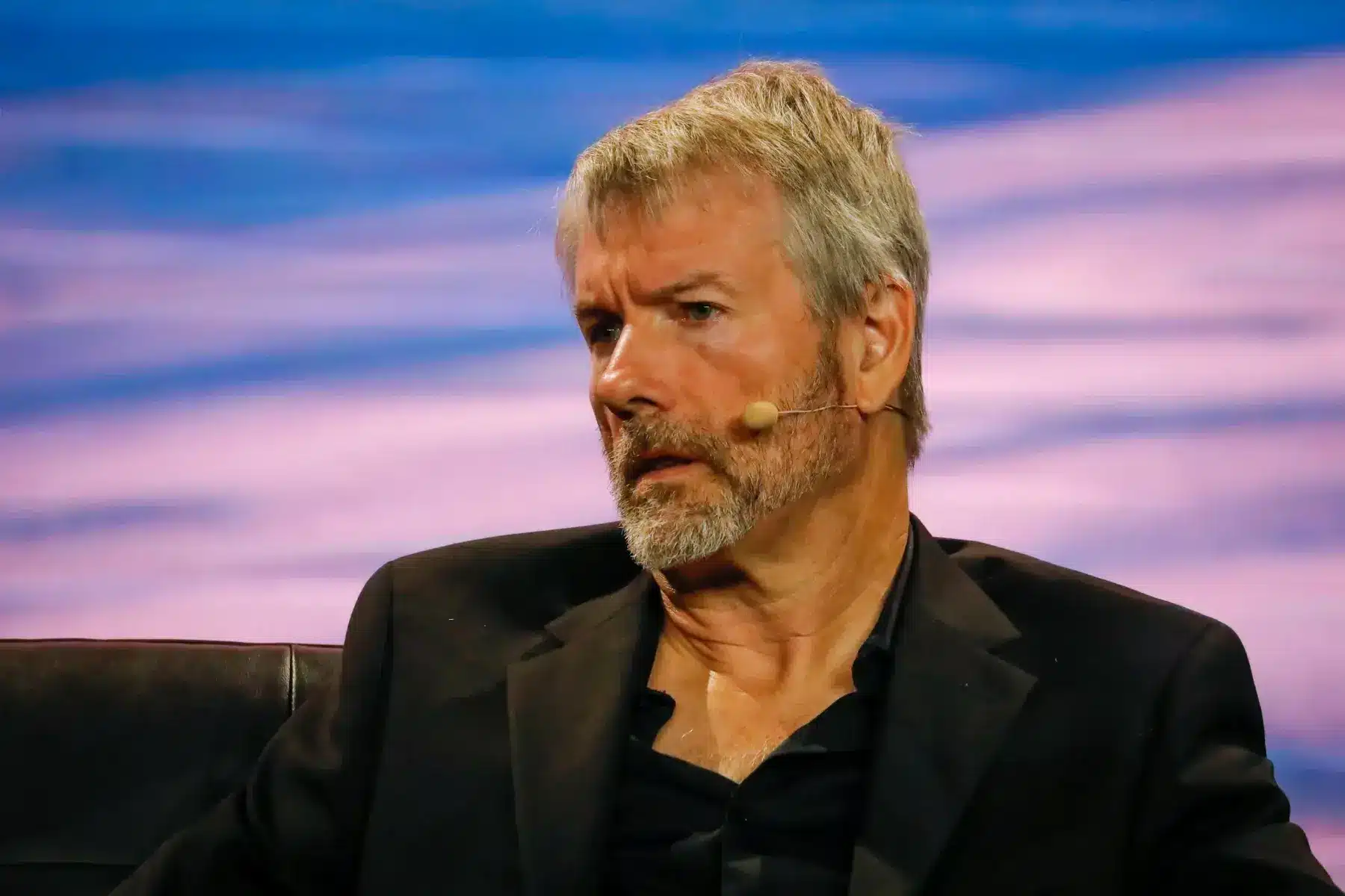 Michael Saylor wearing a black blazer and headset microphone against a blue and purple background