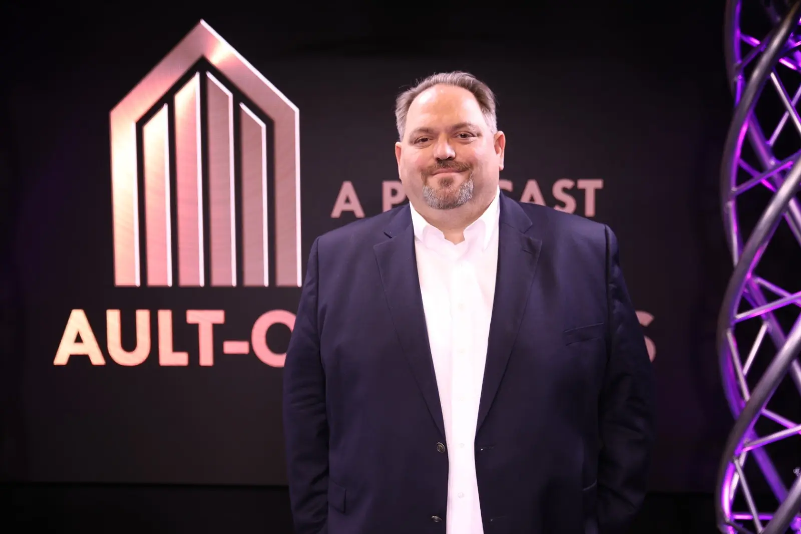 Portrait of Milton Todd Ault III wearing a dark blue suit and white shirt in front of an Ault-Co backdrop.