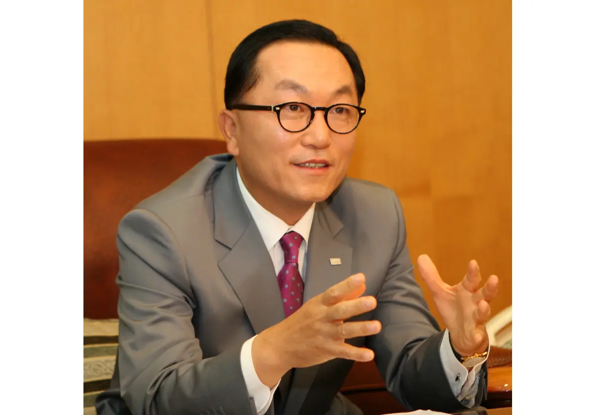 Portrait of Park Hyeon-joo wearing glasses and a grey suit, gesturing with his hands while speaking