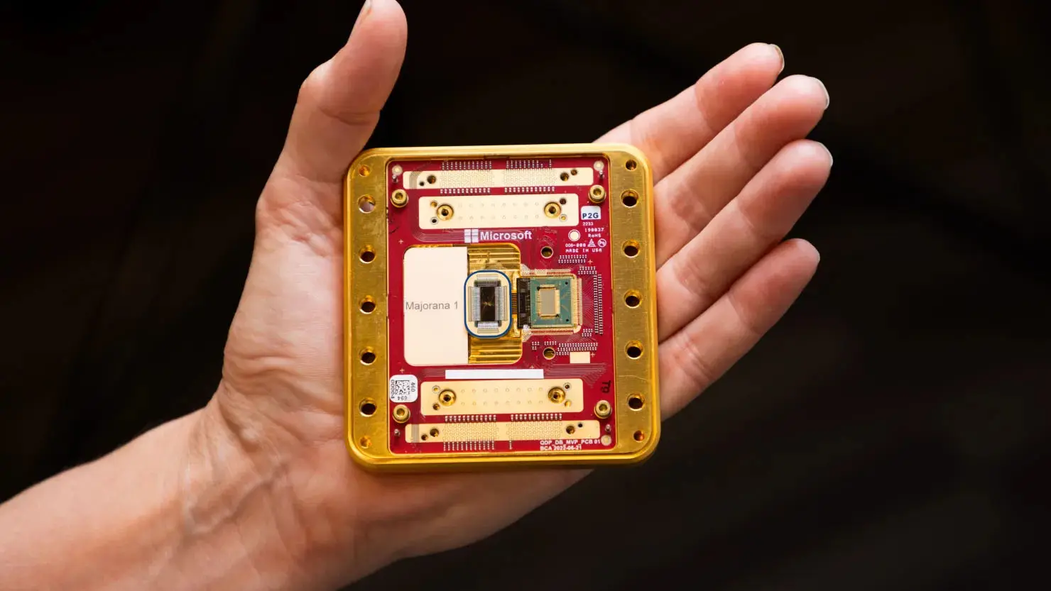 A hand holding the Microsoft Majorana 1 quantum computing processor chip on a red circuit board.