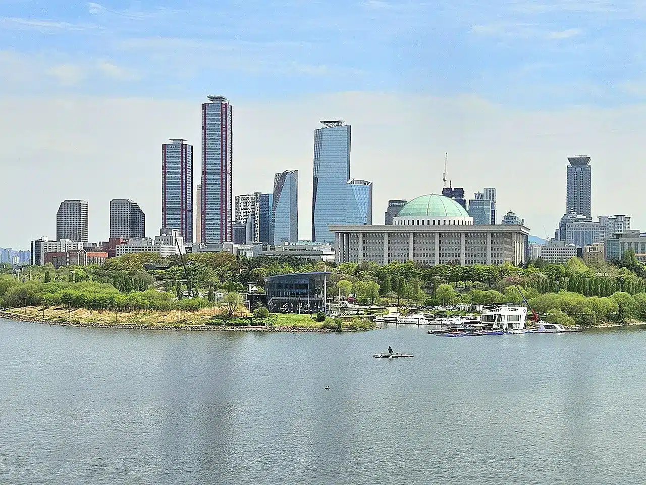 The skyline of Seoul's Yeouido district featuring skyscrapers and the National Assembly Building by the Han River.