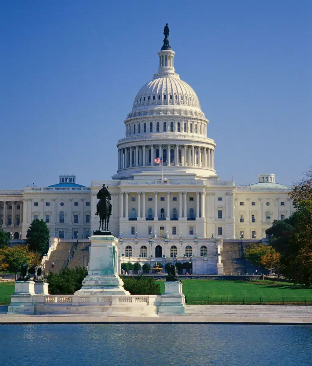 Wide shot of the US Capitol building in Washington DC with a statue in the foreground and a reflecting pool
