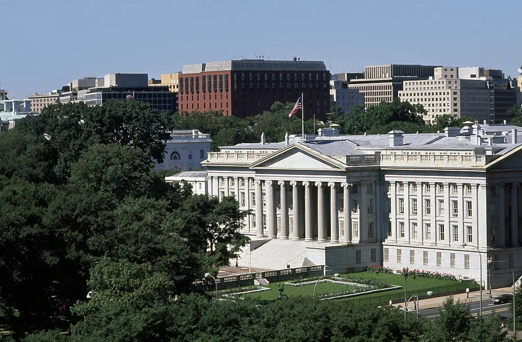 Exterior view of the neoclassical US Department of the Treasury building with white columns and an American flag.