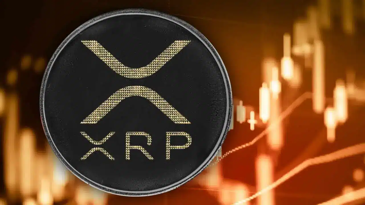 A black physical coin featuring the gold XRP Ripple logo against a blurred gold trading candle chart background