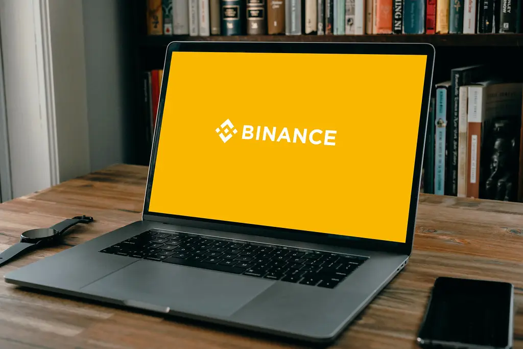 Ein Laptop auf einem Holztisch zeigt das gelbe Logo der Kryptobörse Binance auf dem Bildschirm.