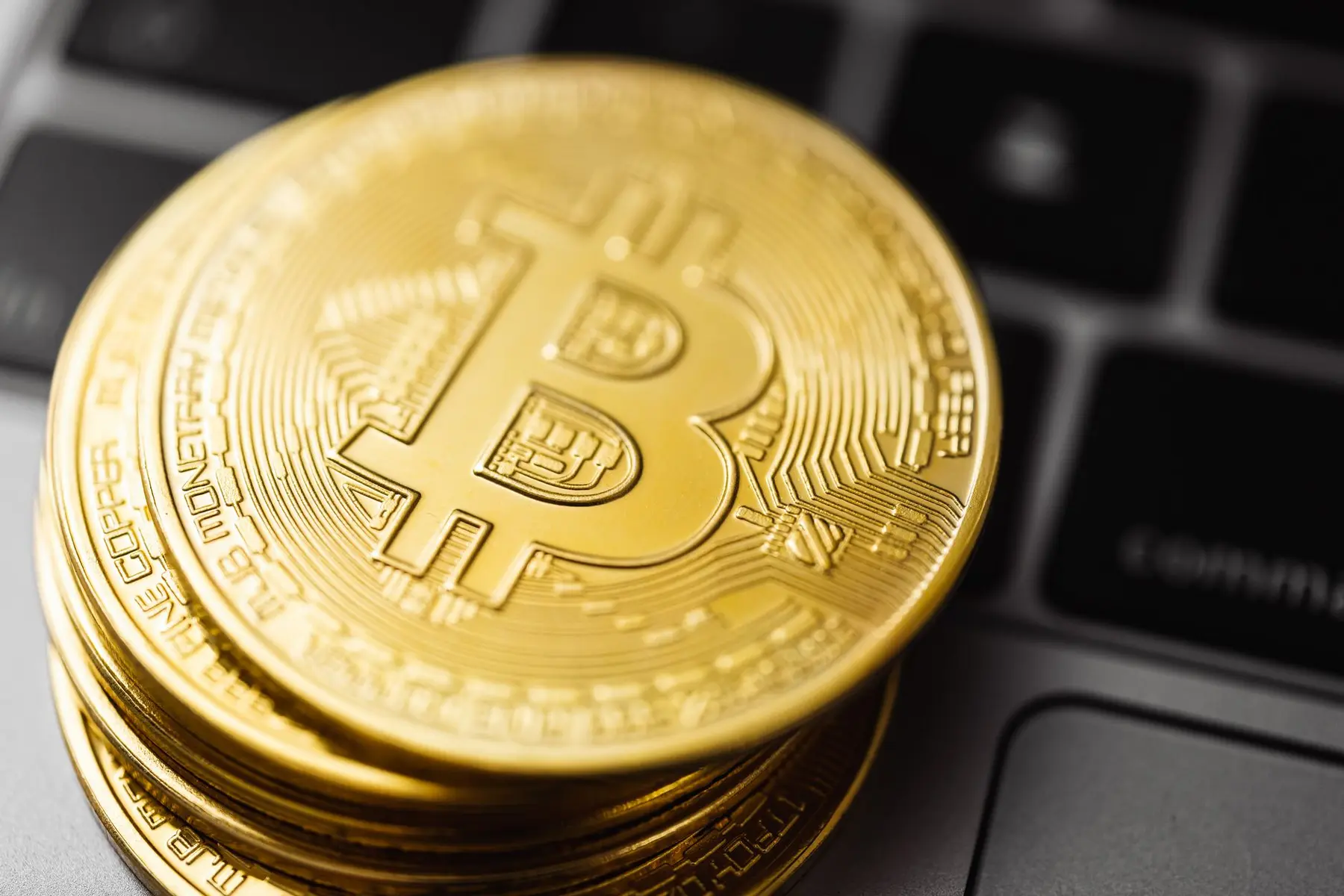 A stack of gold-colored physical Bitcoin coins resting on a laptop keyboard