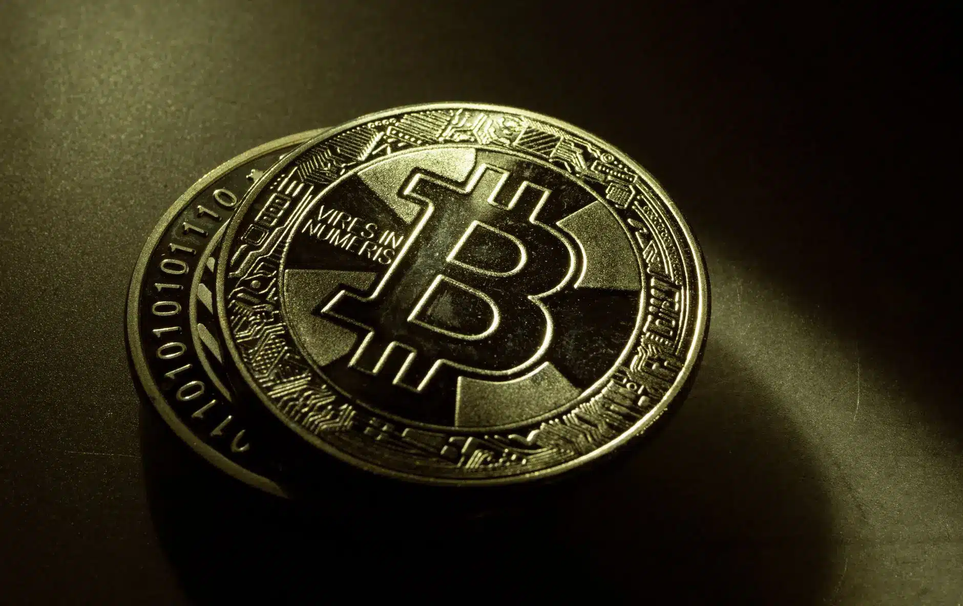 Close-up of two physical gold-colored Bitcoin coins featuring the Bitcoin symbol and binary code