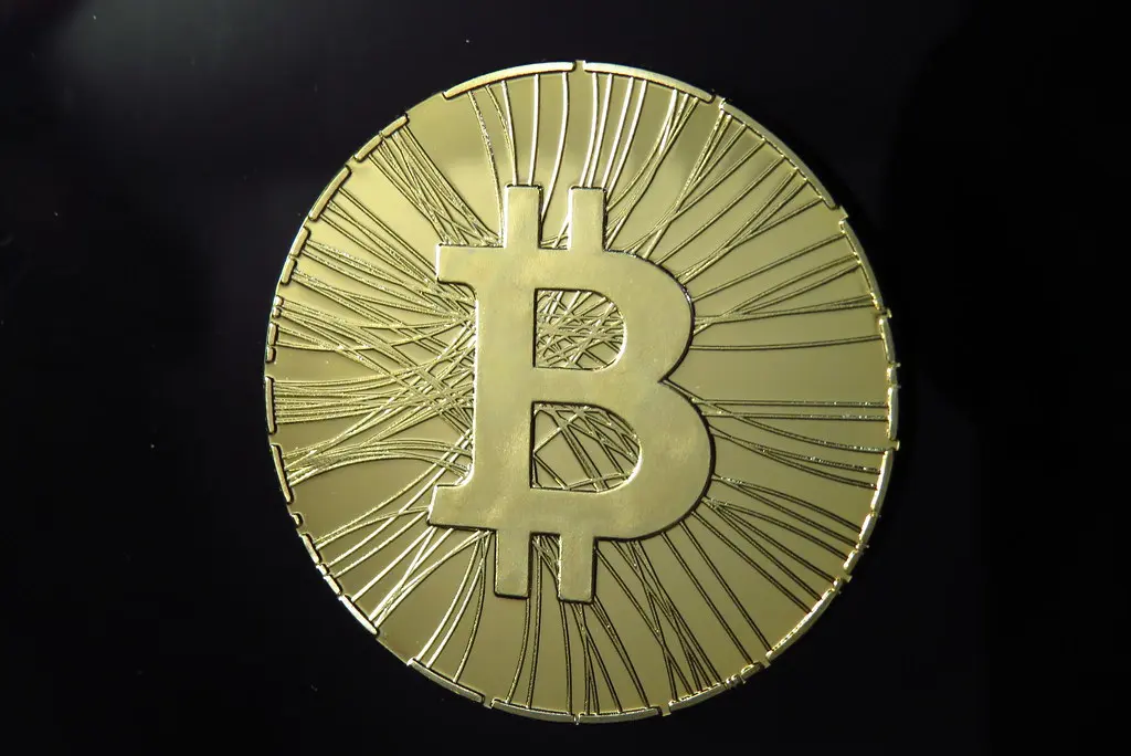 Eine goldene physische Münze mit dem Bitcoin-Logo vor einem schwarzen Hintergrund.