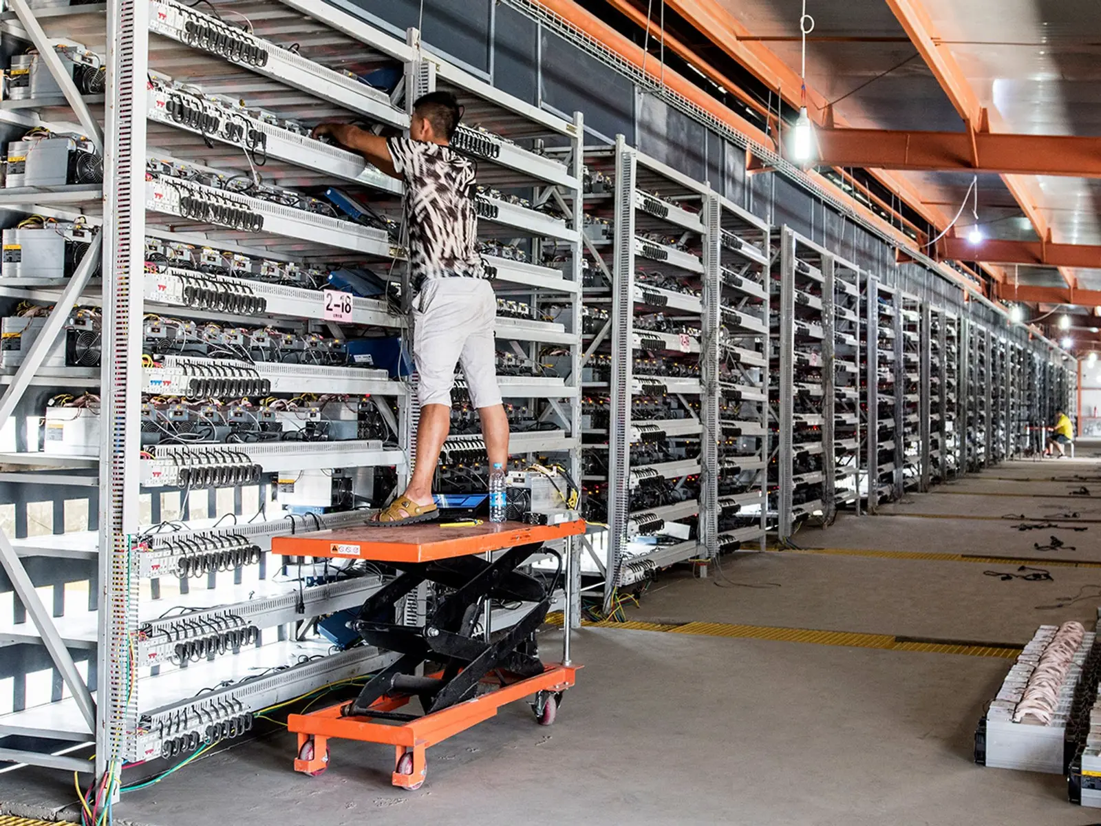 Technician on a lift working on racks of ASIC bitcoin mining hardware in a large data center