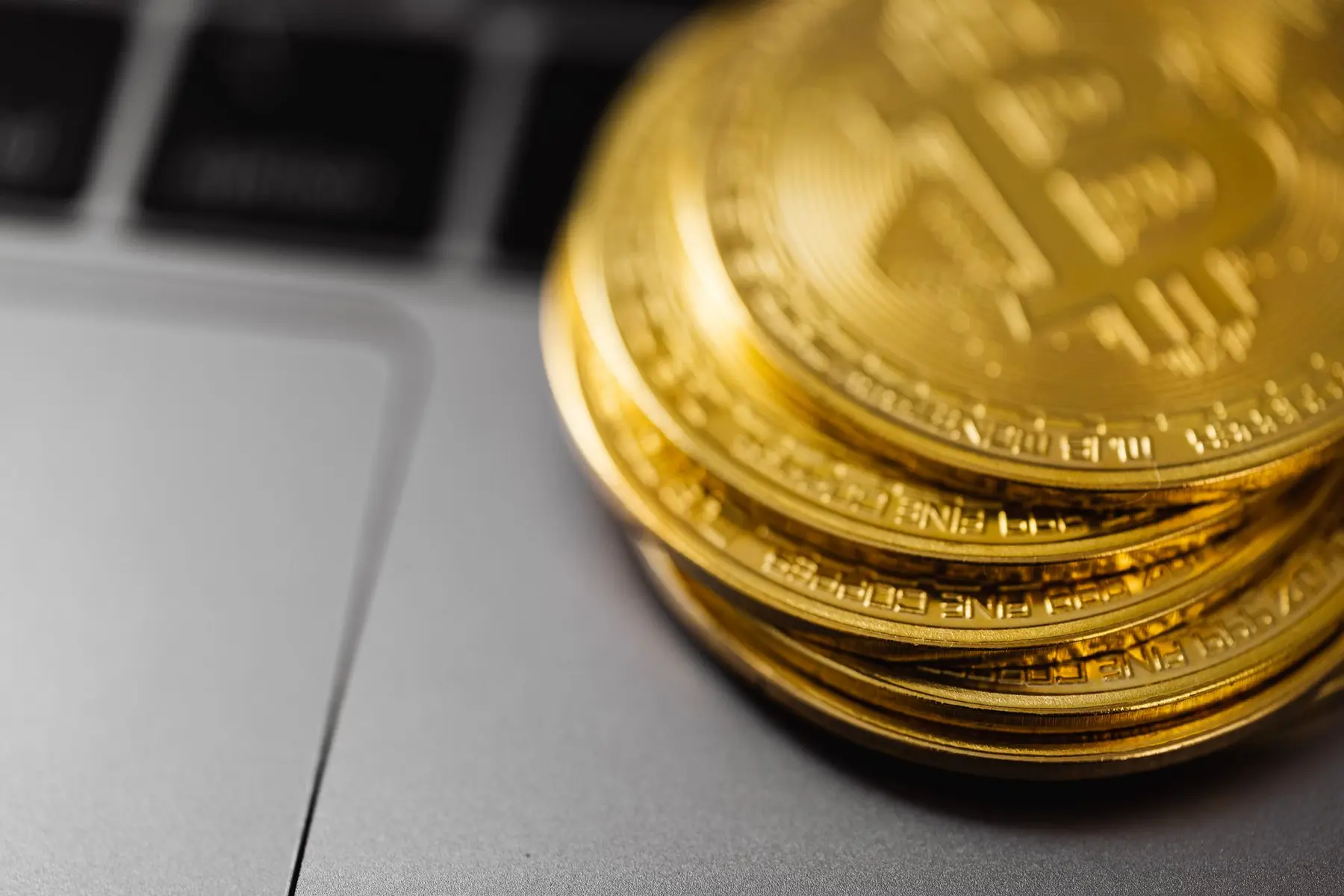 A stack of gold Bitcoin tokens resting on a silver laptop surface