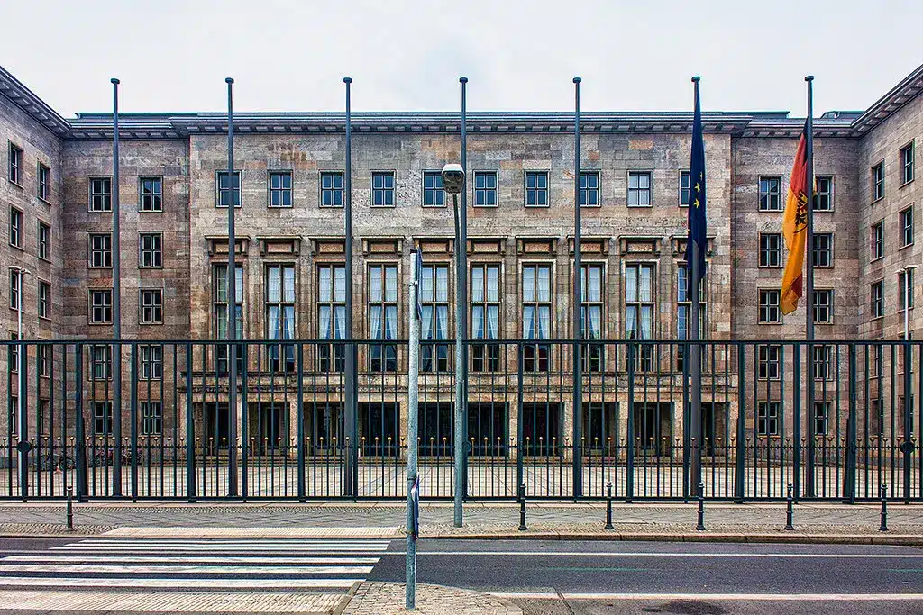Das Gebäude des Bundesministeriums der Finanzen in Berlin mit Flaggen und einem Zaun im Vordergrund.