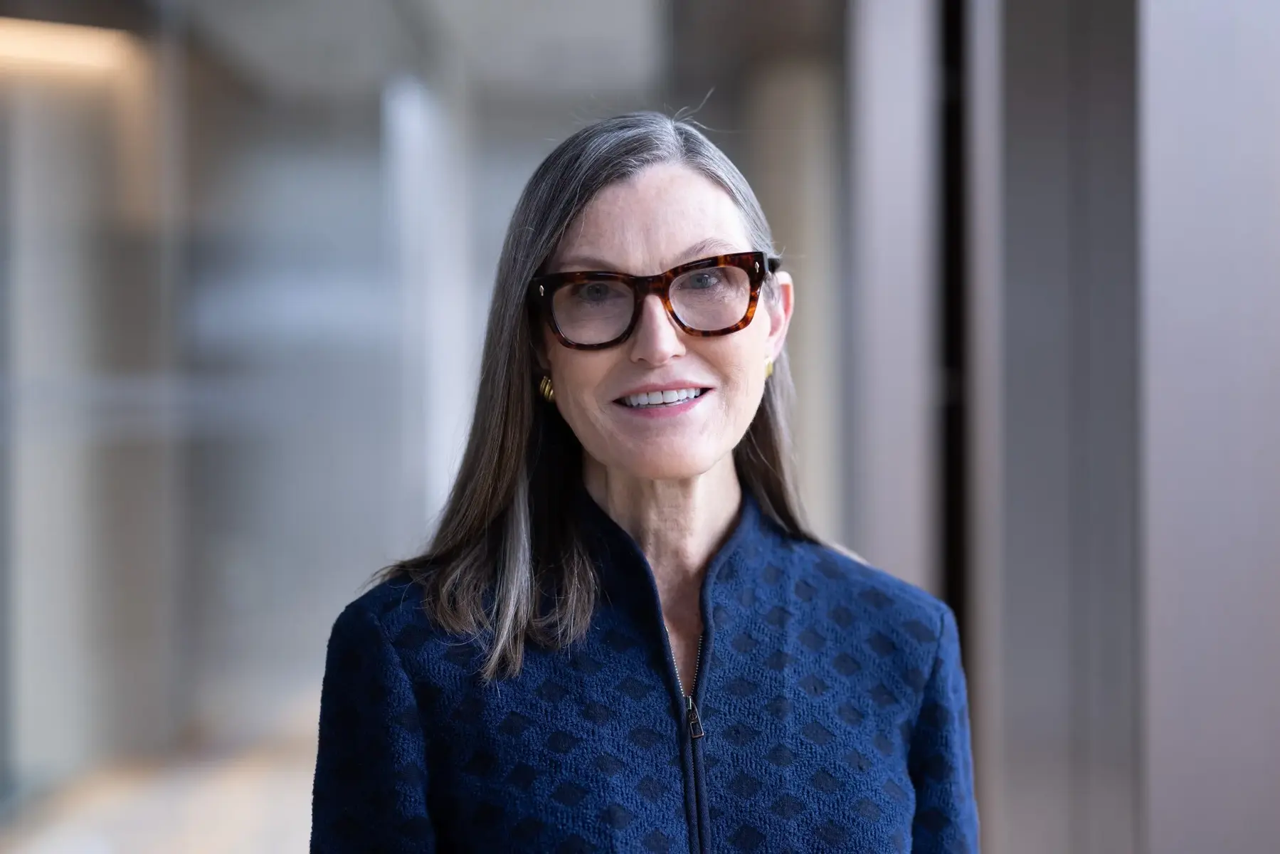Portrait of Cathie Wood wearing glasses and a blue patterned jacket
