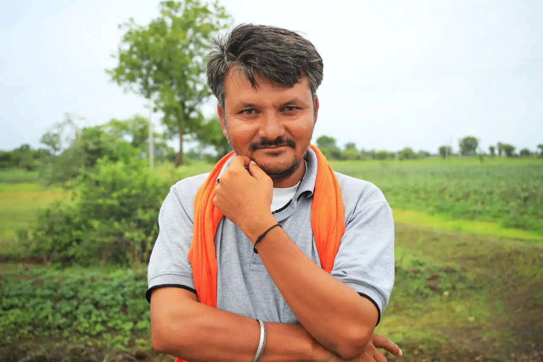 Portrait of Diwakar Choubey wearing a grey polo shirt and orange scarf in a rural field