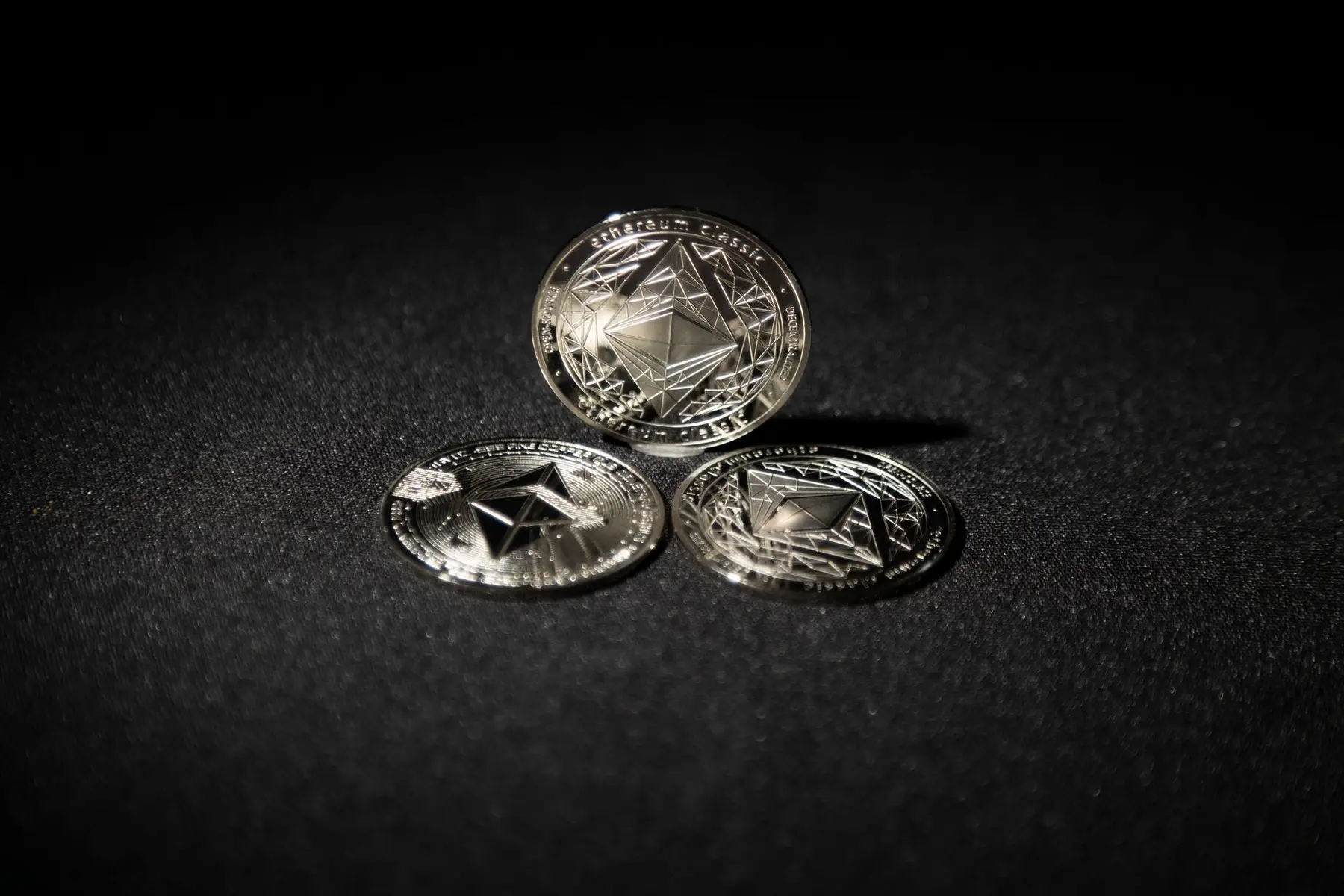Three silver physical Ethereum Classic coins on a dark textured background