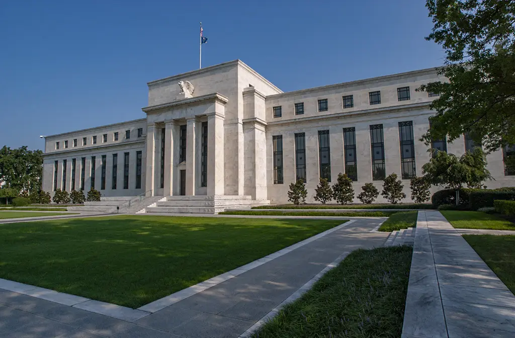 The neoclassical marble facade of the Federal Reserve Board building in Washington DC under a clear blue sky.