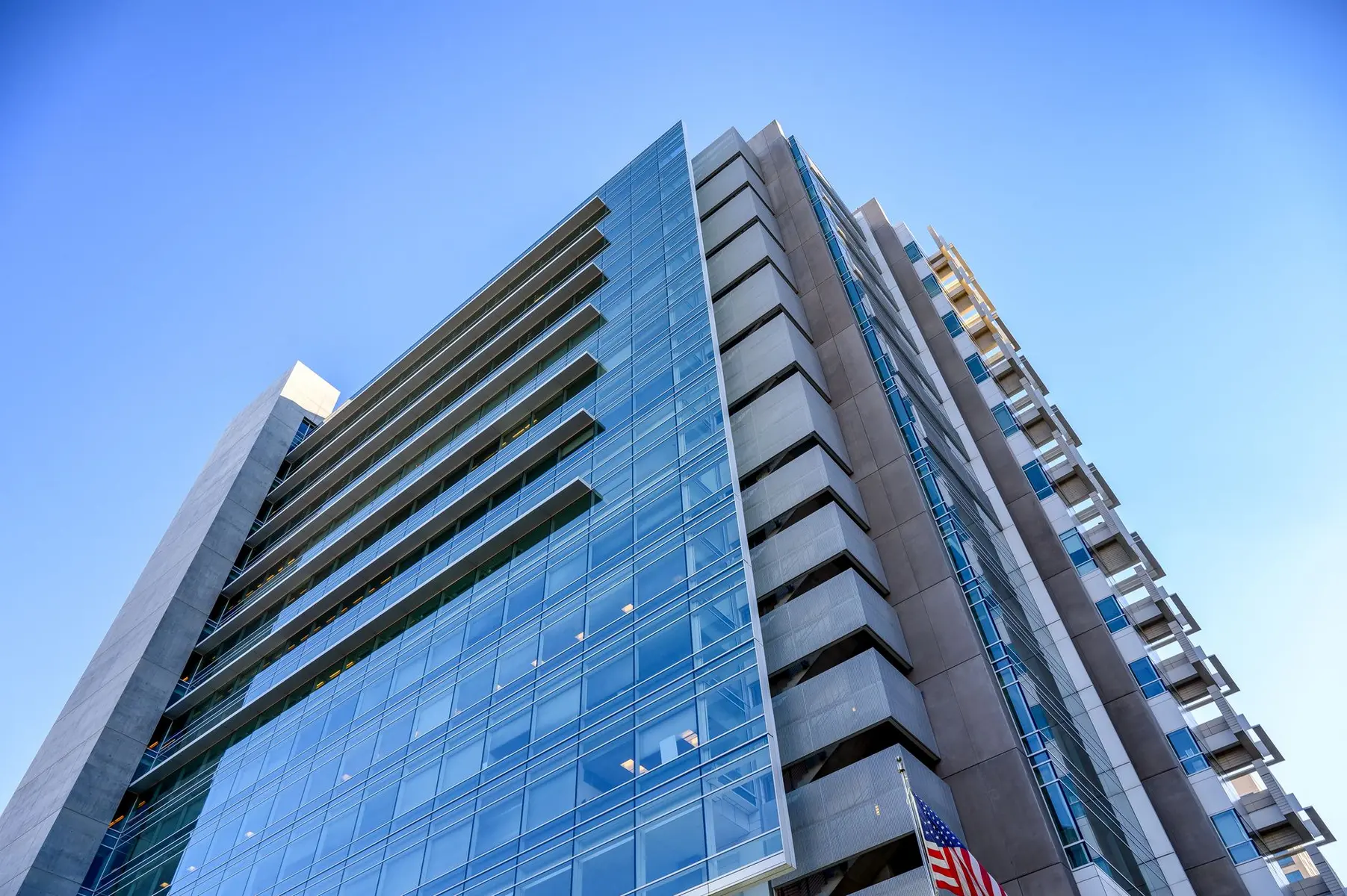Low-angle view of a modern glass and concrete corporate office building against a clear blue sky