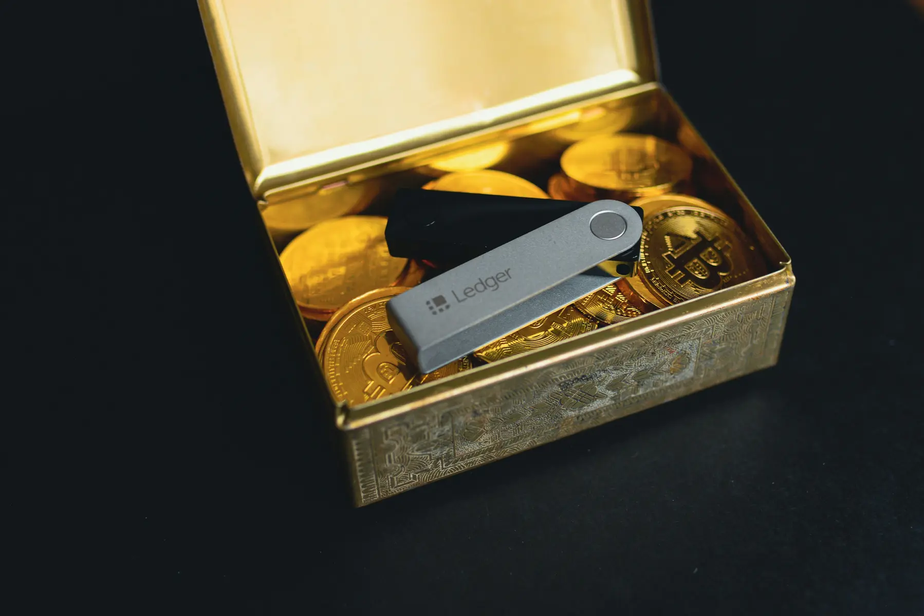 Ein Ledger Hardware-Wallet in einer goldenen Box voller Bitcoin-Münzen