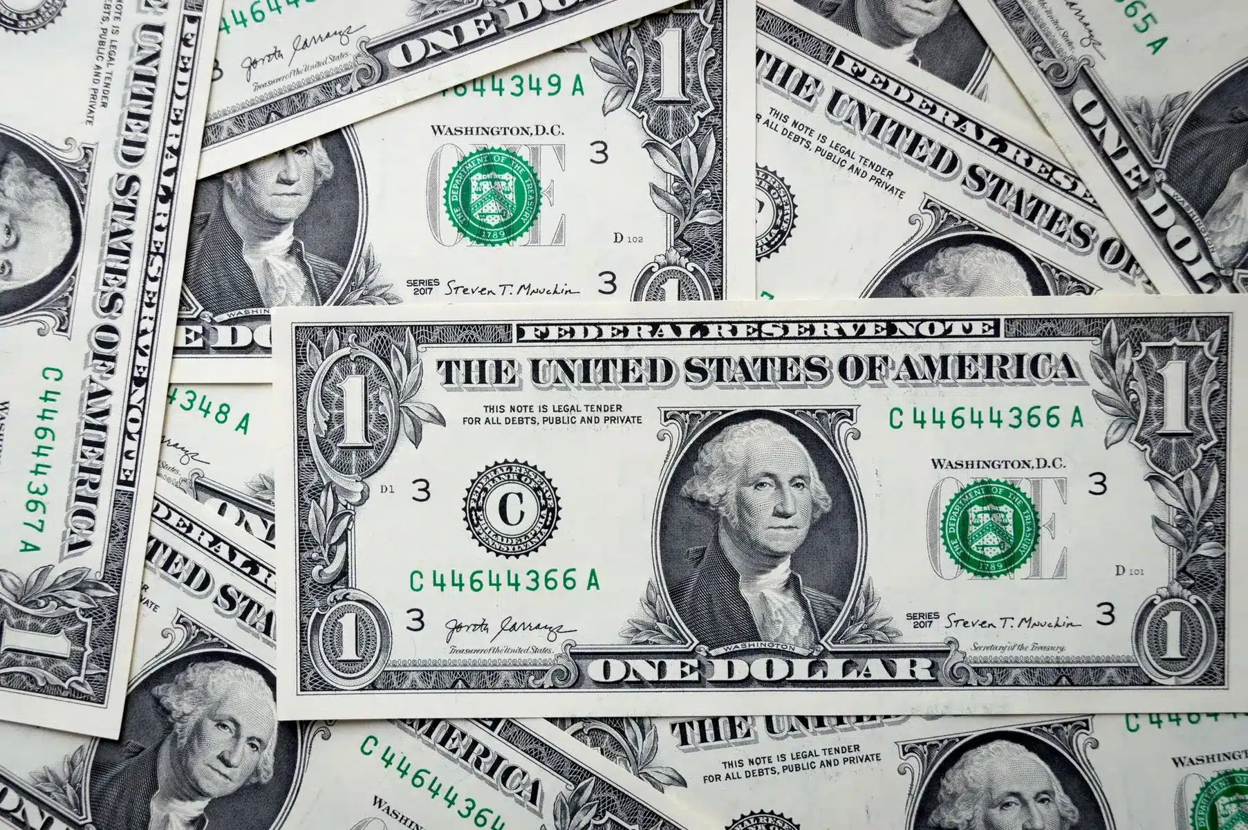 A pile of United States one dollar bills featuring portraits of George Washington.