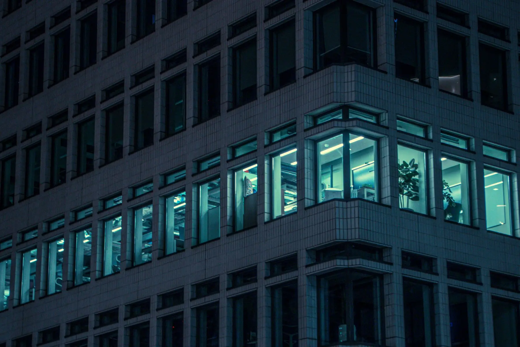 Exterior view of a modern office building at night with lit windows showing interior workspaces