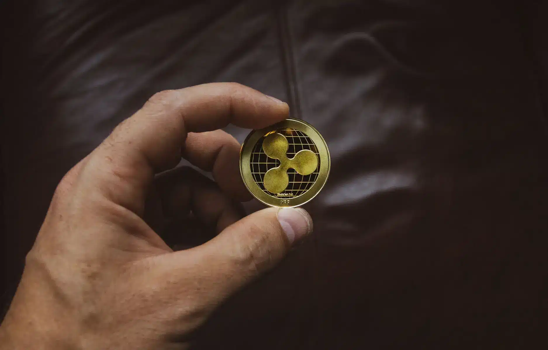 A hand holding a physical gold-colored Ripple XRP cryptocurrency token