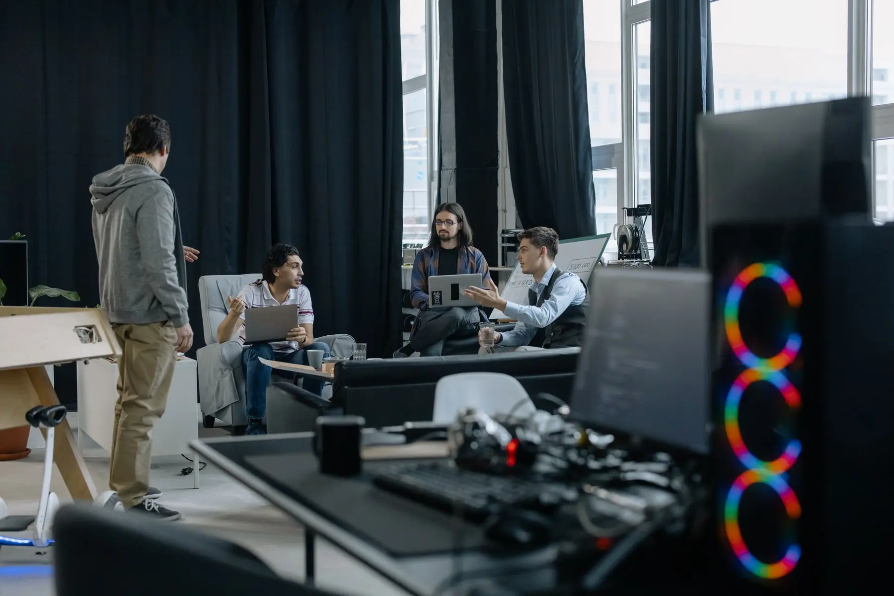 A group of software developers in a modern office discussing a project with laptops
