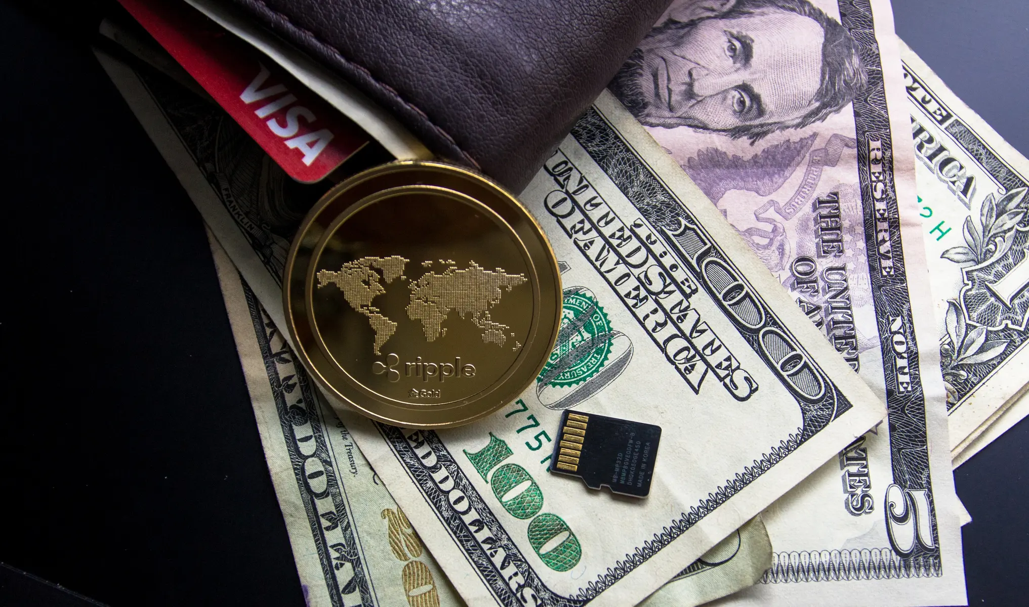 Eine goldene Ripple-Münze auf US-Dollar-Banknoten neben einem Geldbeutel und einer SD-Karte.