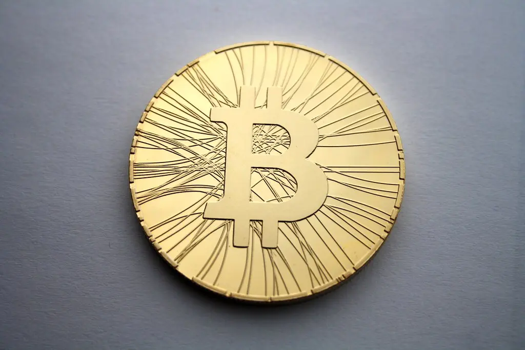 Eine physische goldfarbene Bitcoin-Münze vor einem grauen Hintergrund.