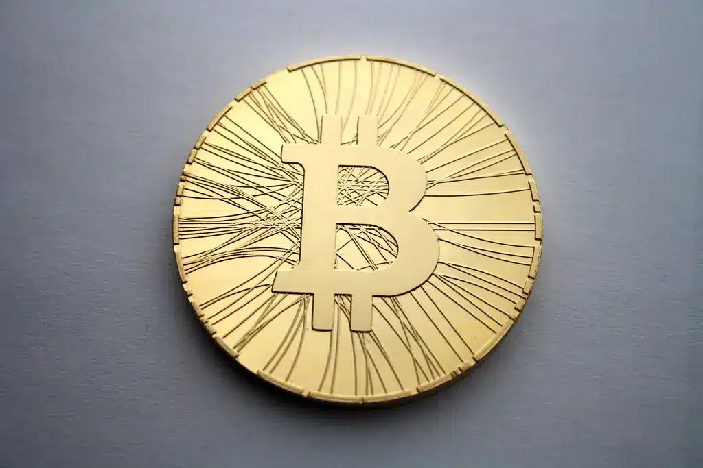 Eine goldene physische Bitcoin-Münze mit dem Bitcoin-Logo auf einem grauen Hintergrund.