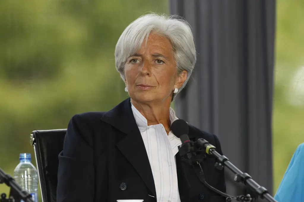 Porträt von Christine Lagarde in einem dunkelblauen Blazer und weißer Bluse vor einem unscharfen grünen Hintergrund.