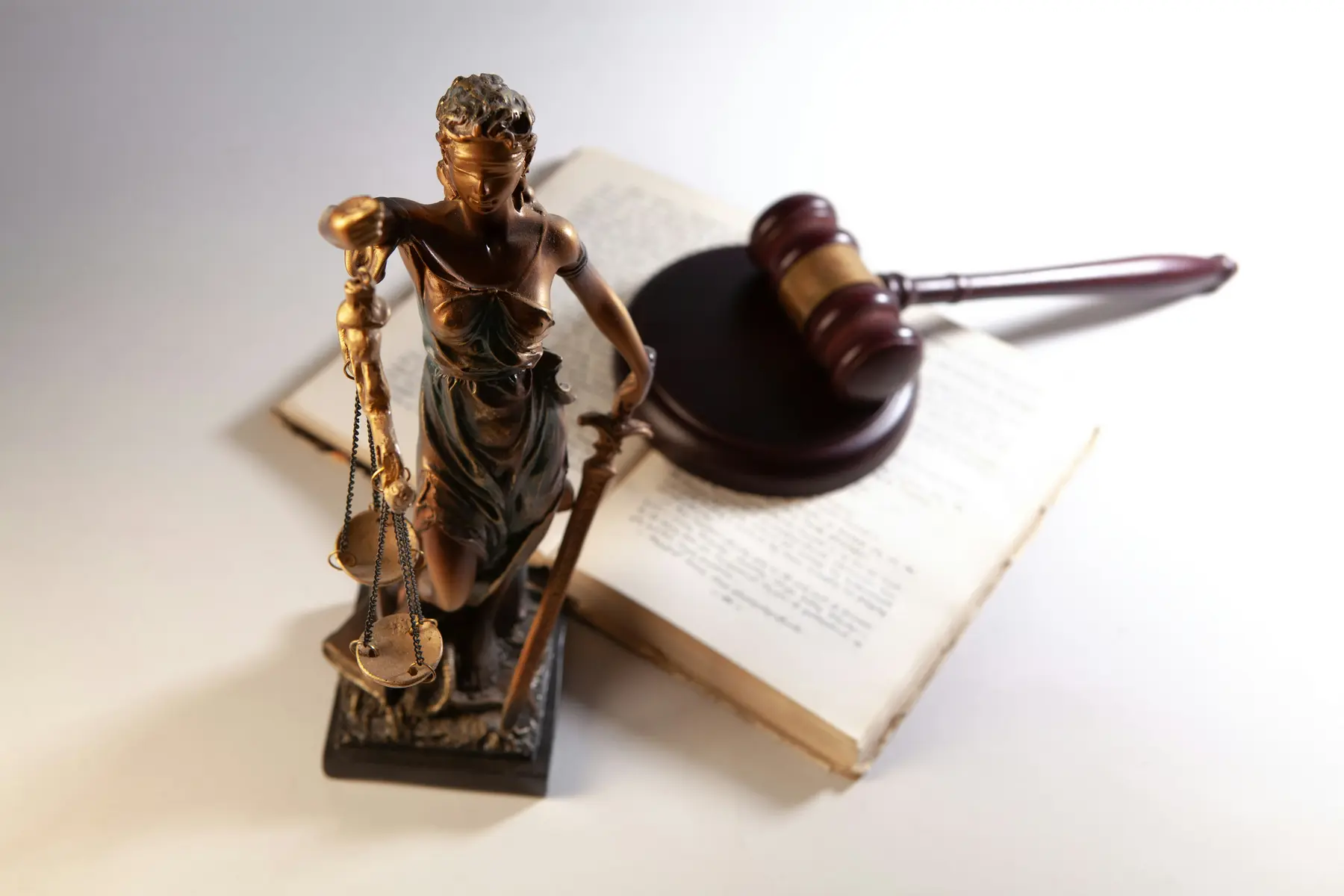 Justitia-Statue, Richterhammer und ein aufgeschlagenes Buch auf weißem Hintergrund
