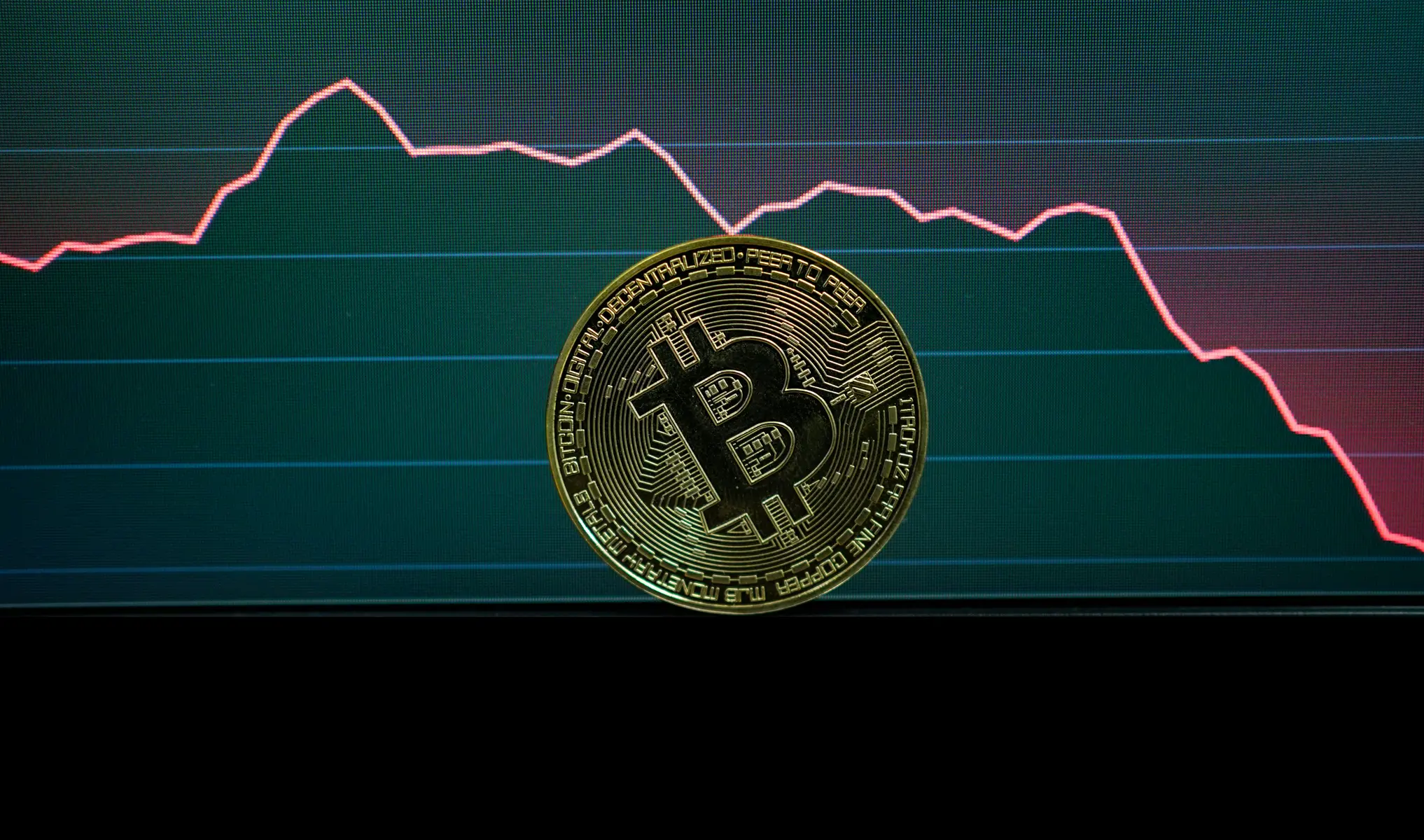 Eine goldene Bitcoin-Münze vor einem Bildschirm mit einem fallenden Kursdiagramm.