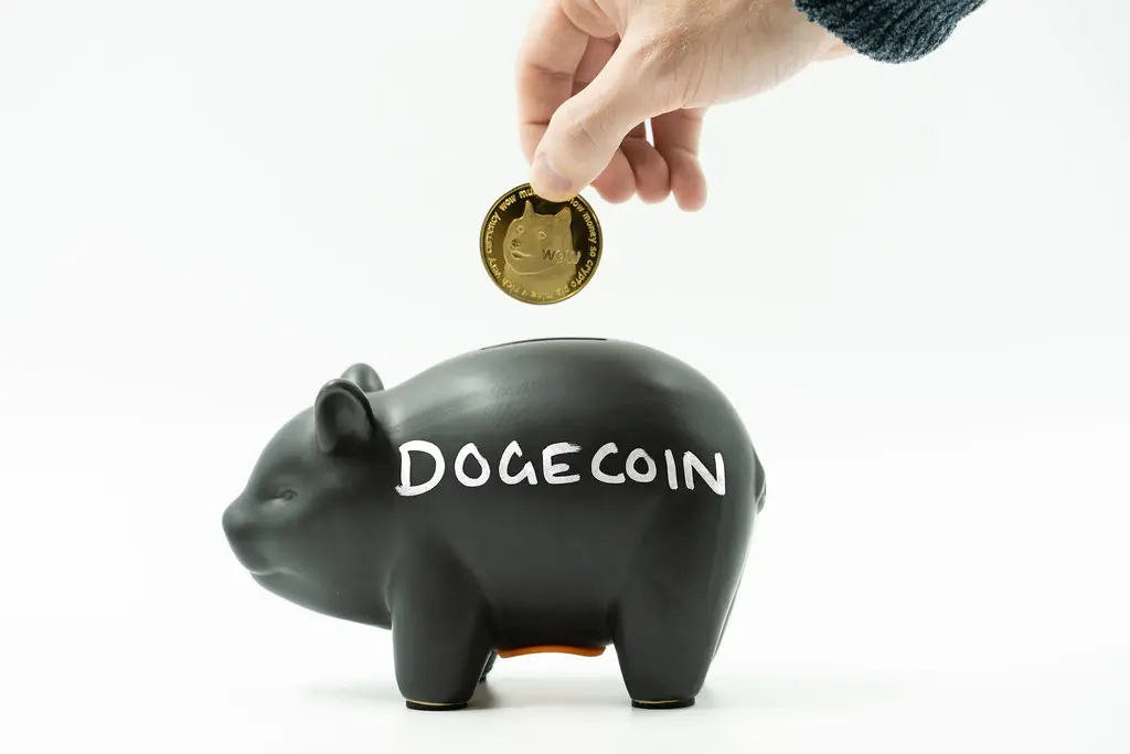 Eine Hand legt eine goldene Dogecoin-Münze in ein schwarzes Sparschwein mit der Aufschrift Dogecoin.