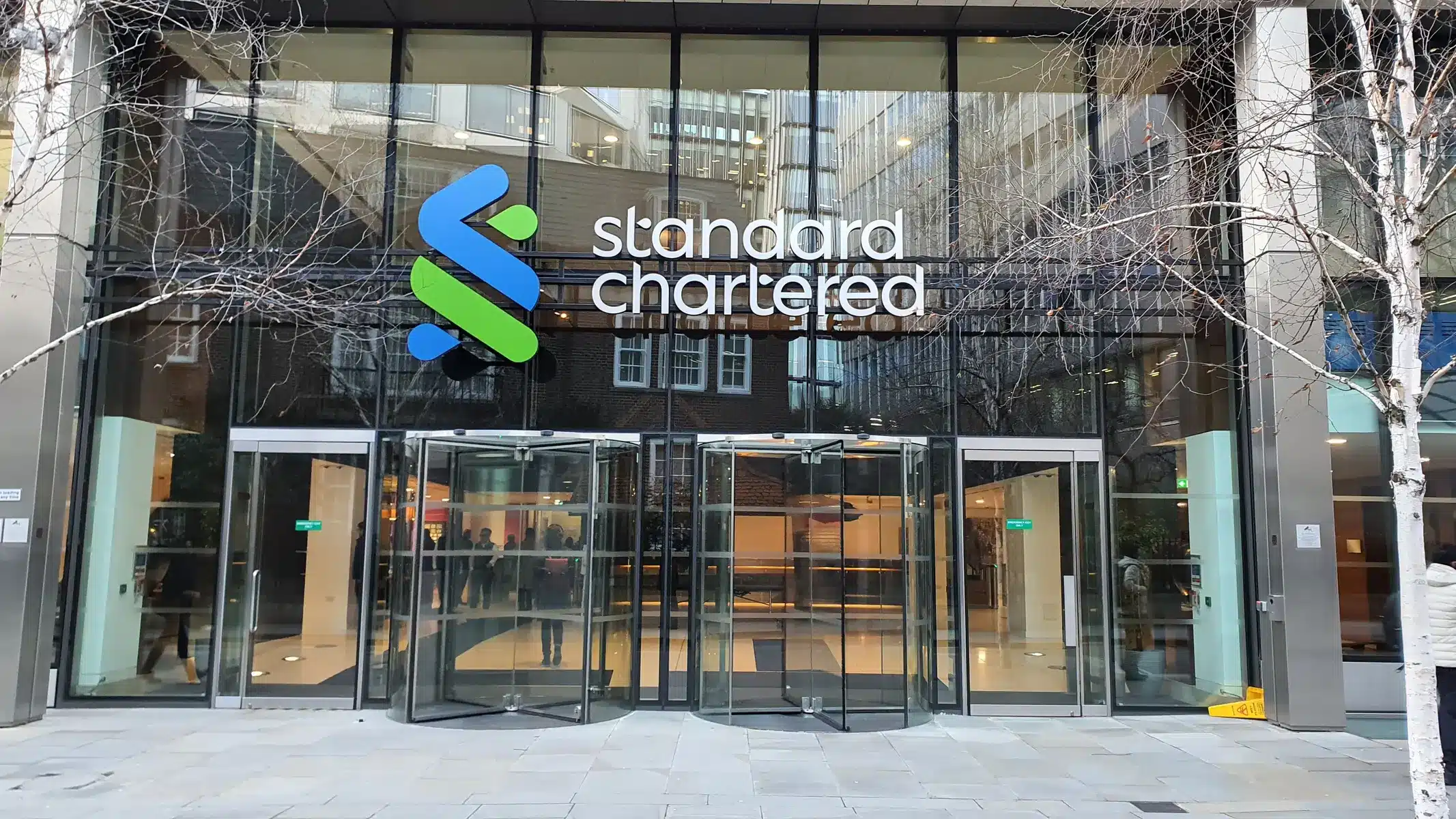 Die gläserne Außenansicht des Hauptsitzes von Standard Chartered mit dem Firmenlogo über dem Eingang.