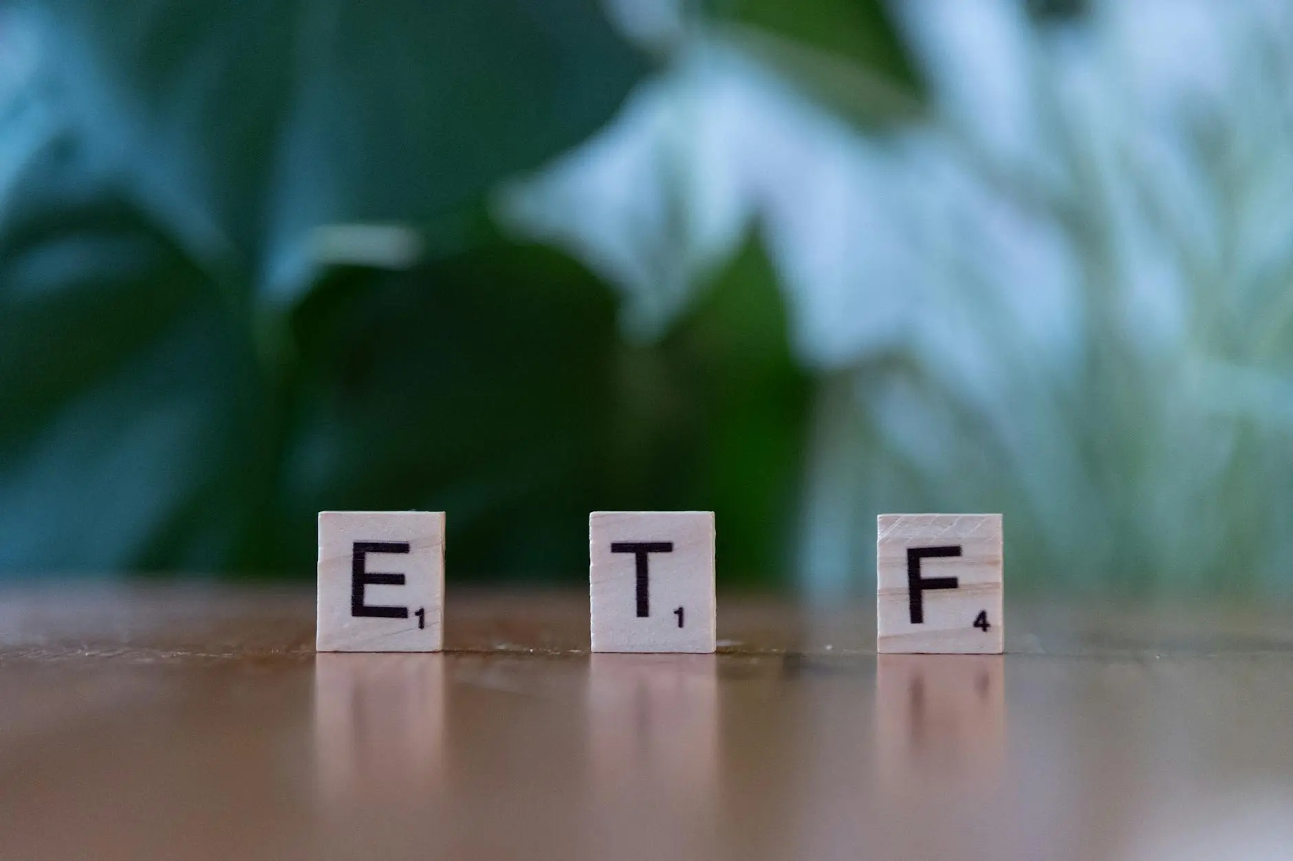 Wooden blocks spelling 'ETF' on a wooden surface with green foliage in the background.
