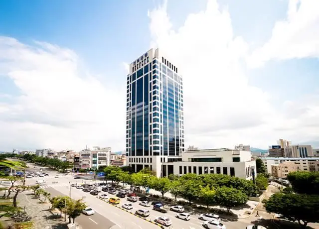 The tall, modern glass and white facade of the Jeonbuk Bank headquarters building under a blue sky.